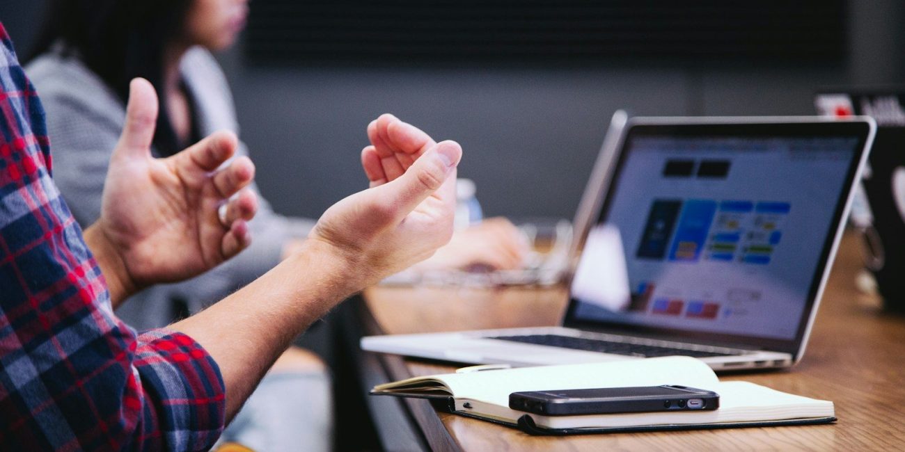 person gesturing during meeting with laptop
