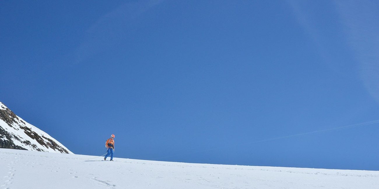 Person walking on snow under a clear blue sky.