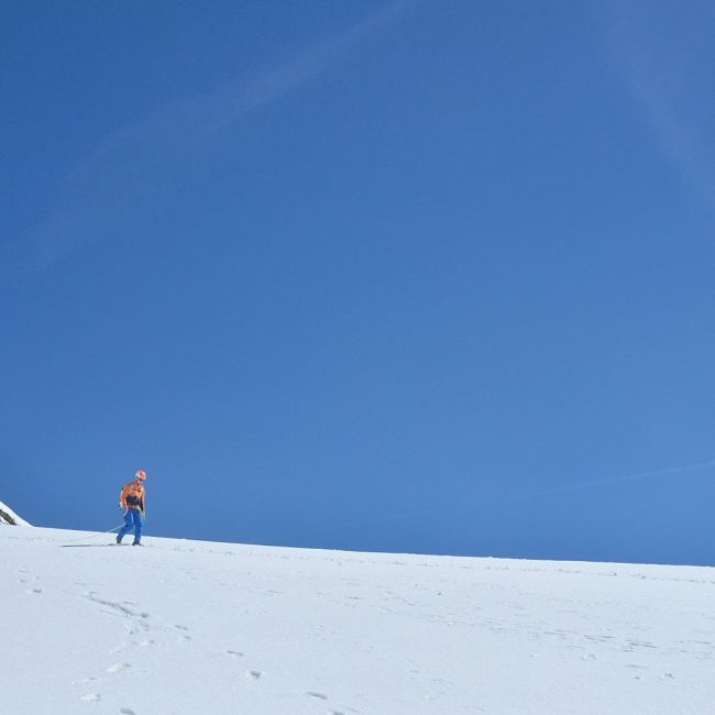 Person walking on snow under a clear blue sky.